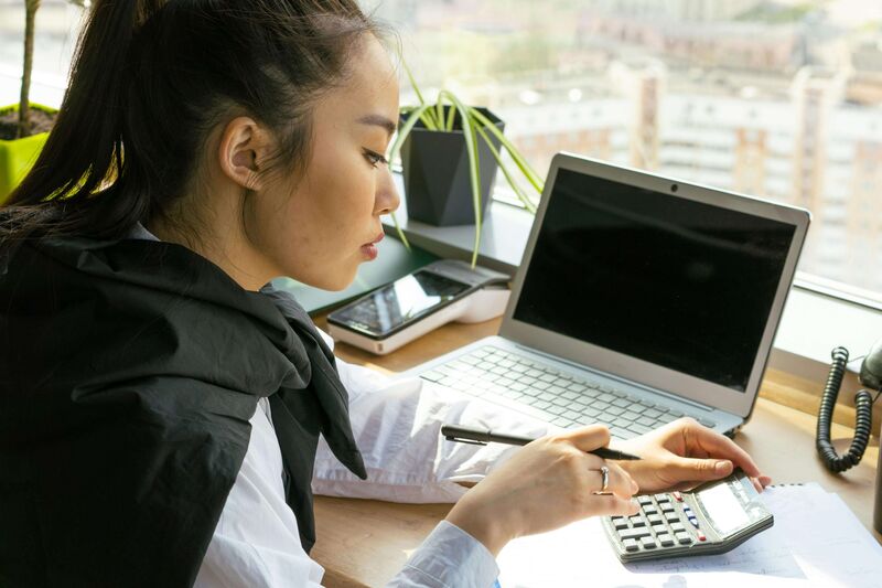 Woman using a calculator at a desk with a laptop — representing affordable website pricing.