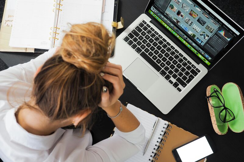 Small business owner frustrated by website problems, holding head in hands while working at desk
